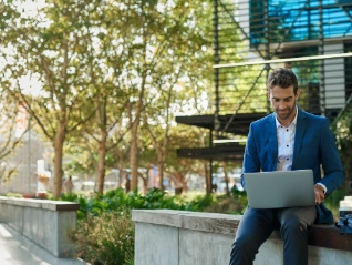 young businessman working online with laptop sitting outside