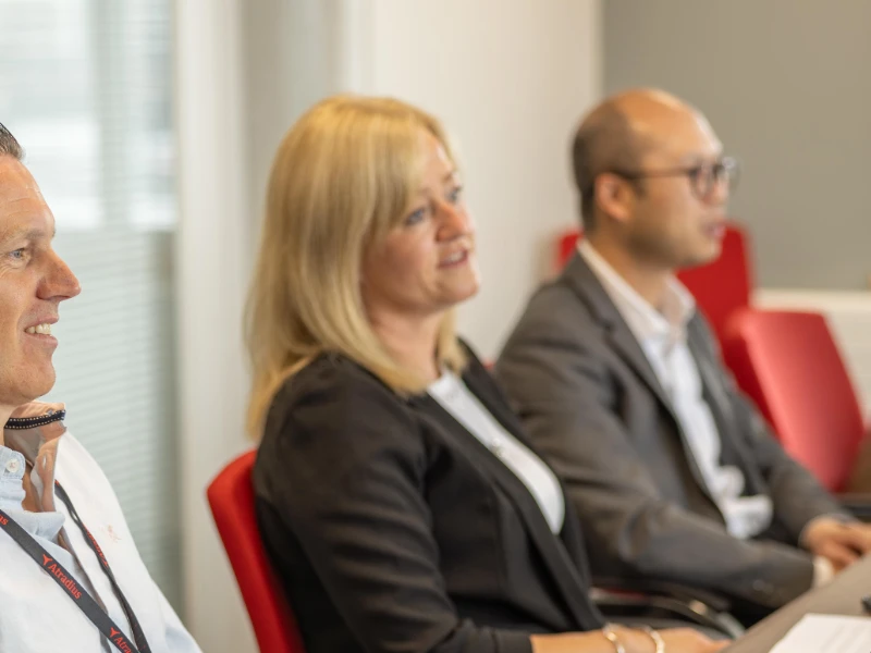 Two women and men in a large meeting room